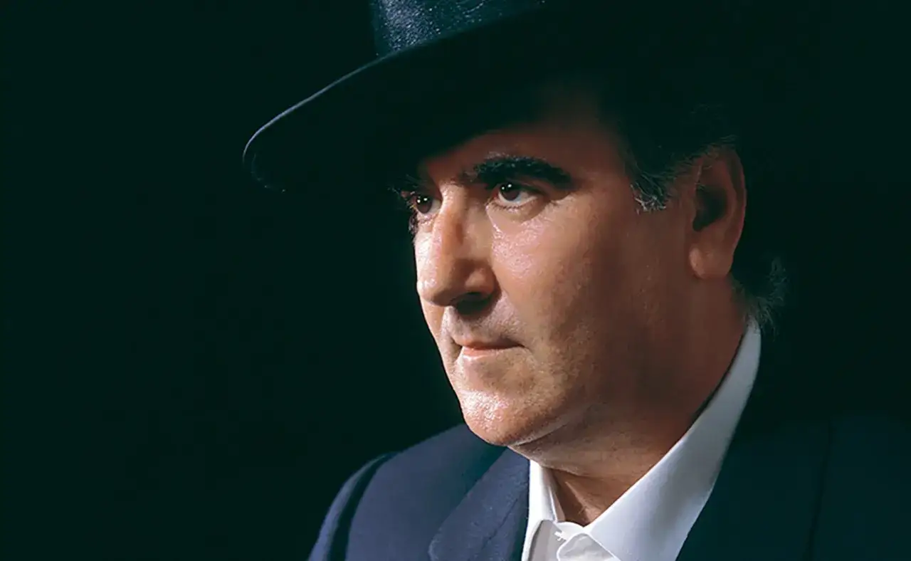 Retrato de un cantante sevillano flamenco con sombrero negro y traje oscuro.