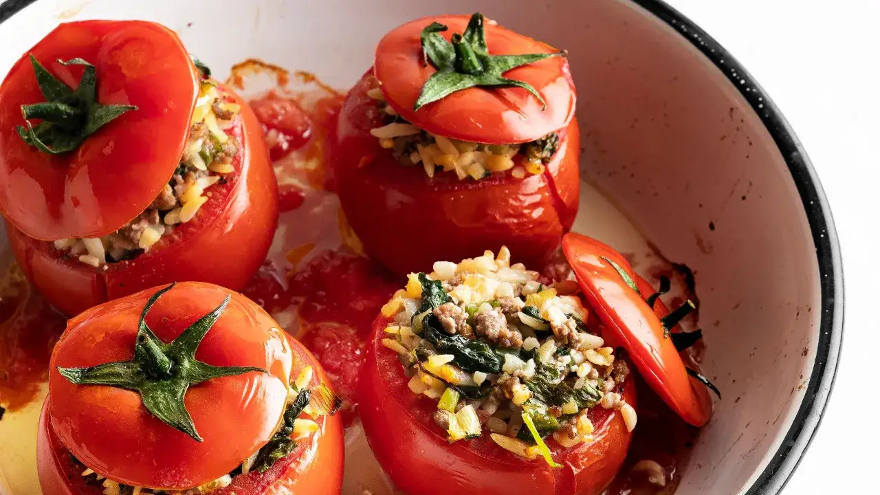 Pomodori ripieni cotti al forno, con un gustoso ripieno di riso, carne macinata e verdure, serviti in una teglia.