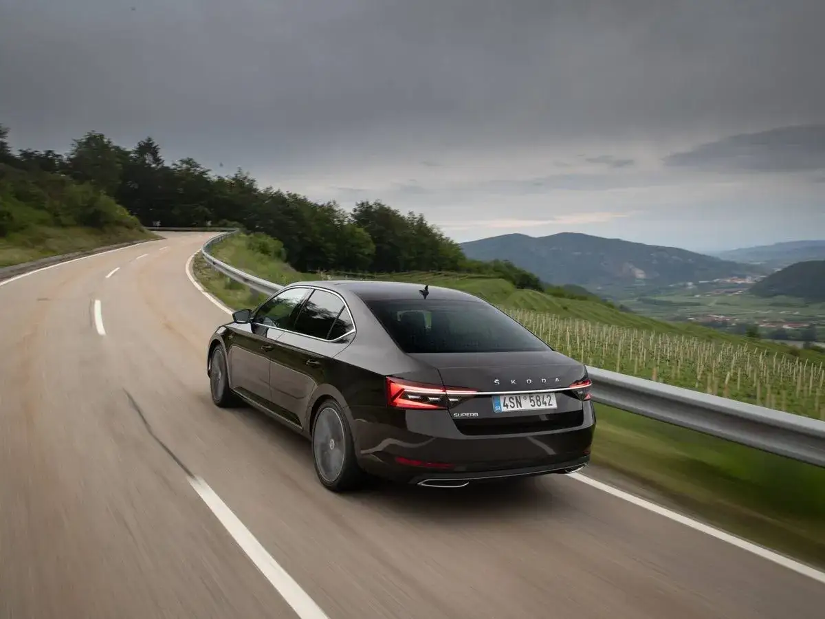 Coche oscuro en carretera sinuosa, con vi&ntilde;edos y monta&ntilde;as al fondo. El **combustible de motor** impulsa este viaje esc&eacute;nico.