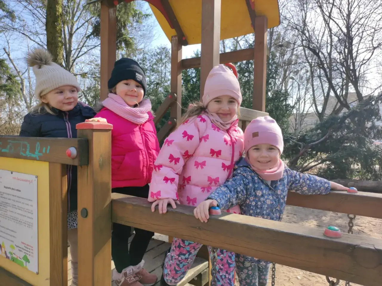 Cztery uśmiechnięte dziewczynki na placu zabaw, czekające aż zostaną otwarte place zabaw dla dzieci.