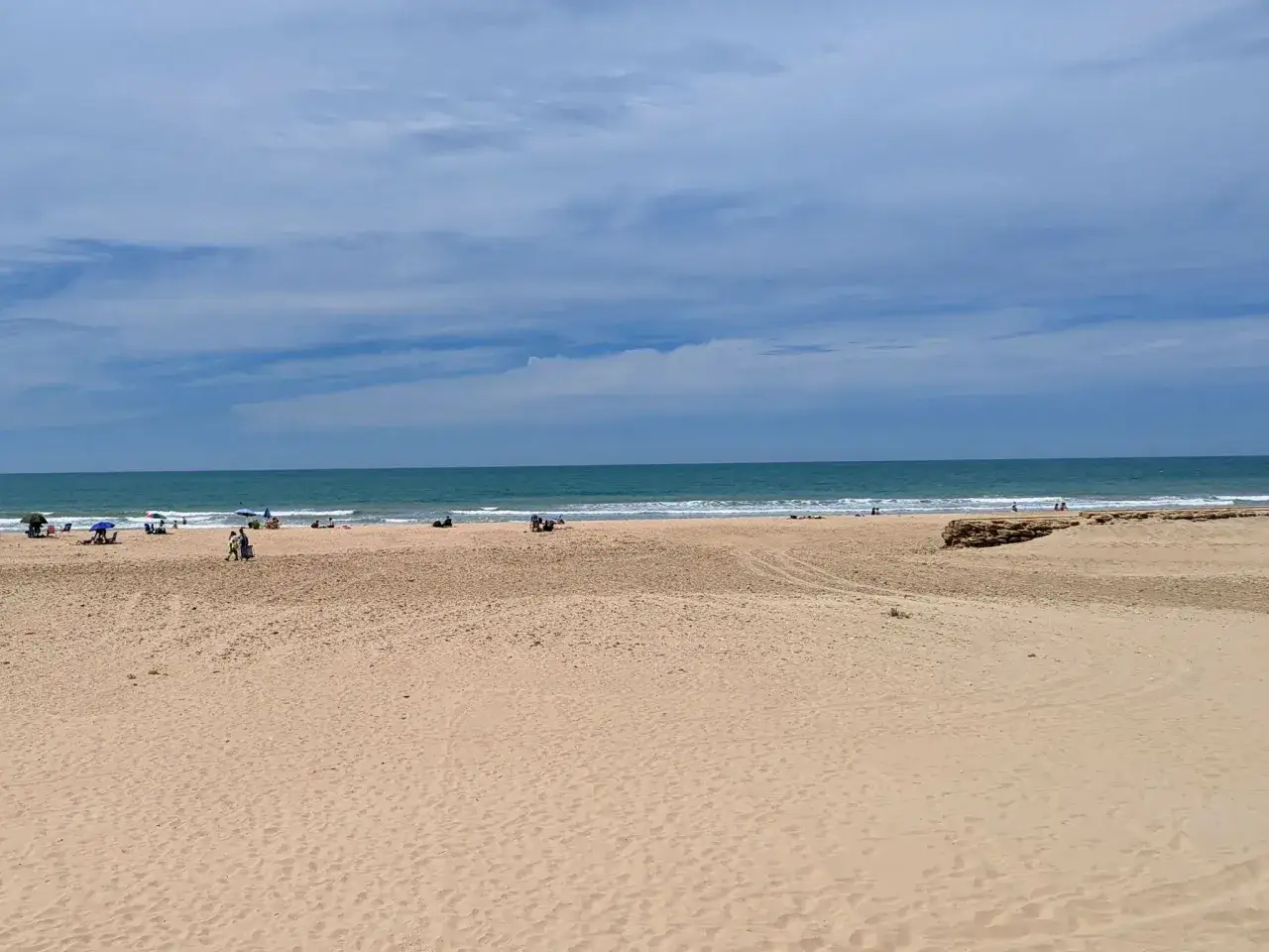 Ein sonniger Tag am playa de cortadura. Menschen entspannen sich am Sandstrand, w&auml;hrend sanfte Wellen das Meer s&auml;umen.