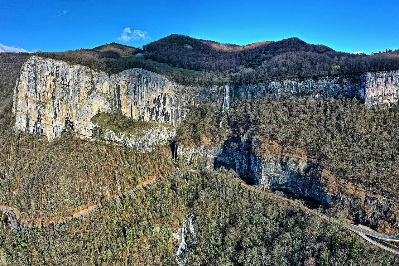 Vue aérienne de la cascade de Syratus, impressionnante chute d'eau tombant d'une falaise rocheuse, entourée de forêts denses.