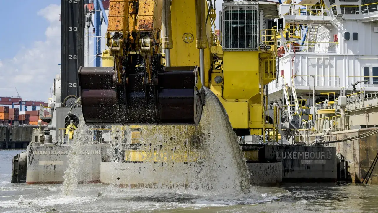 Gelbe Baggerschiff-Arme entleeren Schlamm ins Wasser. Ein riesiger Eimer schaufelt Material aus dem Fluss.