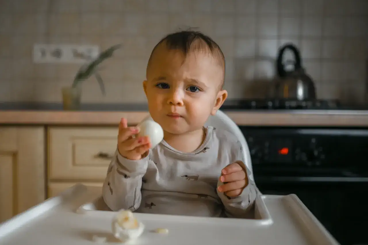 Un bébé d'un certain âge tient un œuf dur, prêt à le déguster.