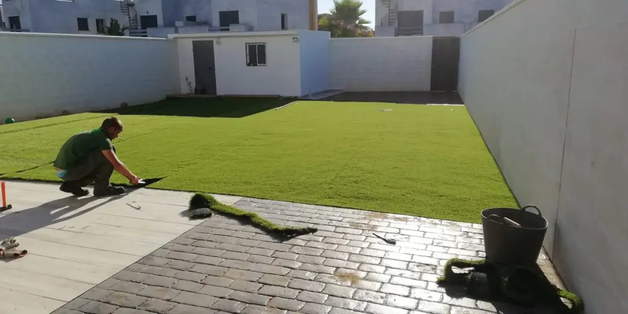 Hombre instalando césped artificial en un patio. Un ejemplo de como colocar césped artificial para un acabado perfecto.
