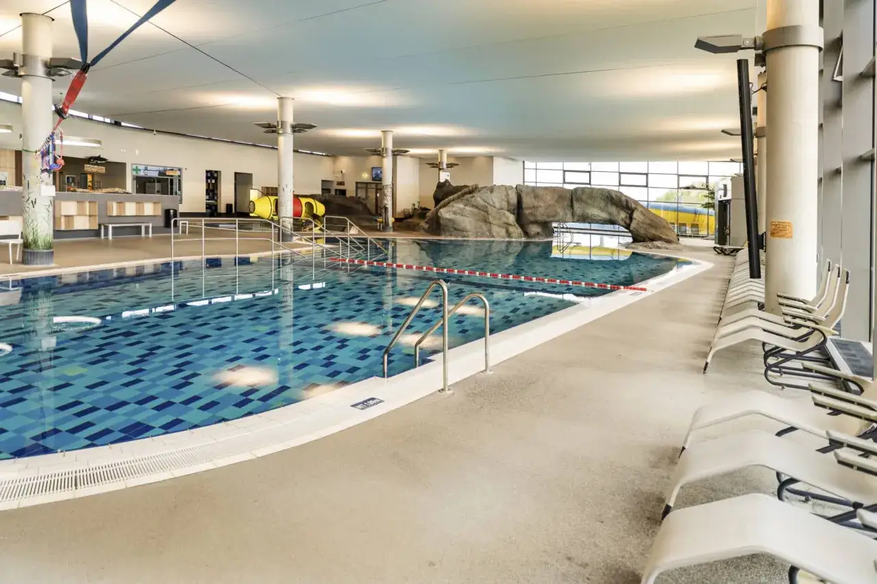 Ein großes Schwimmbecken mit blauen Kacheln und einer Felswand-Attraktion. Hier ist das perfekte Erlebnisbad Ostsee für die ganze Familie.