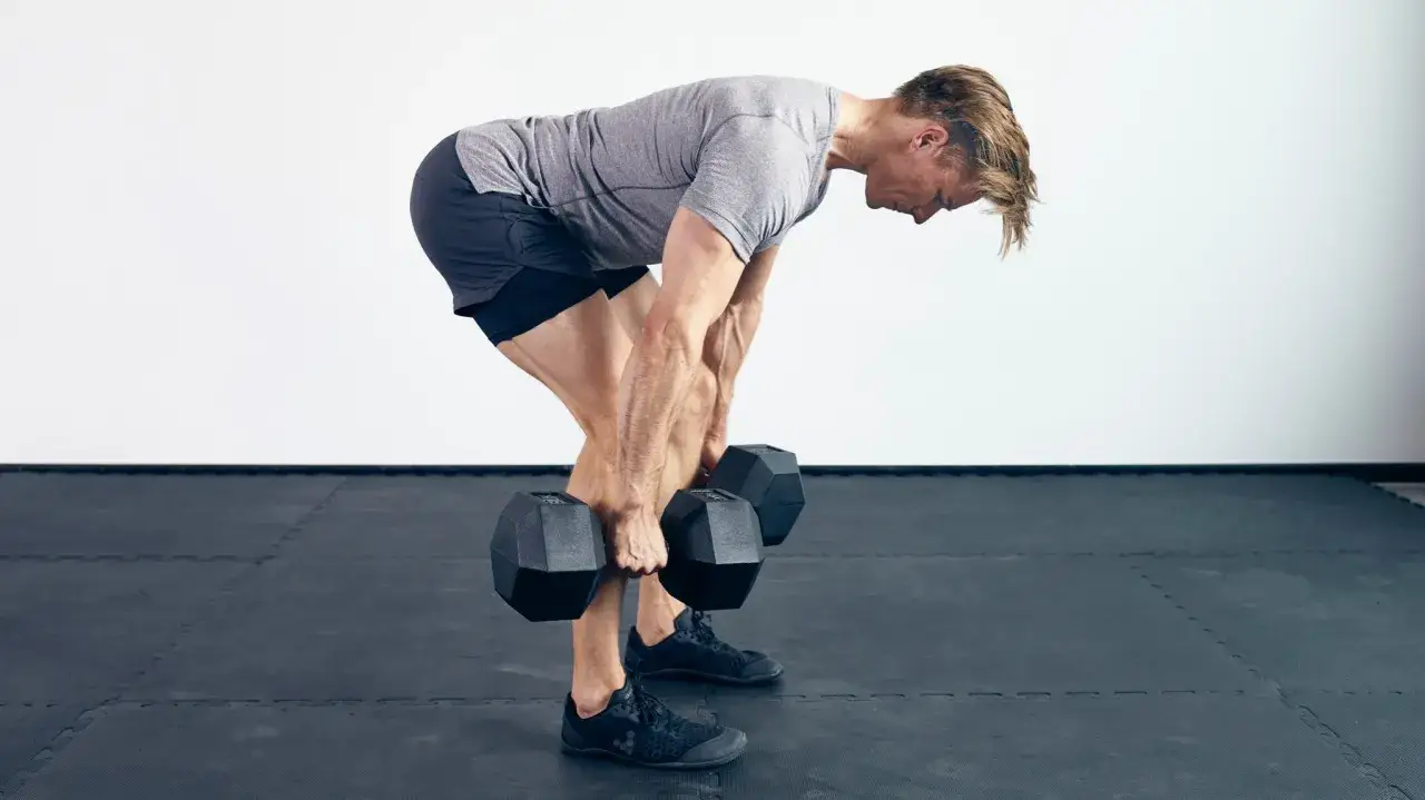 Homme faisant un **dead lift** avec des haltères, dos courbé, jambes fléchies, concentré sur son effort.