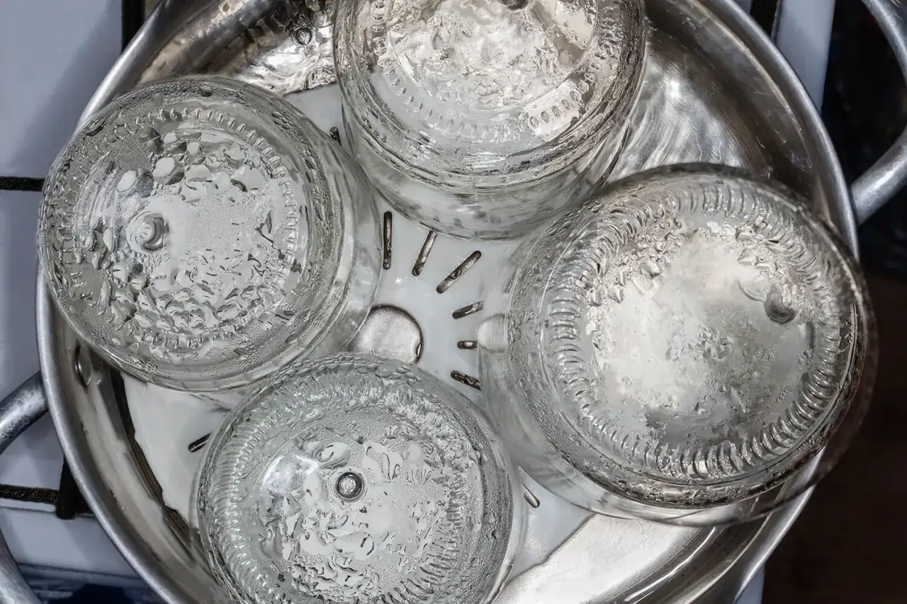 Vier leere Glasflaschen werden in einem Dampfgarer gestapelt, um sie zu sterilisieren. Wassertropfen bilden sich auf den Glasfl&auml;chen.