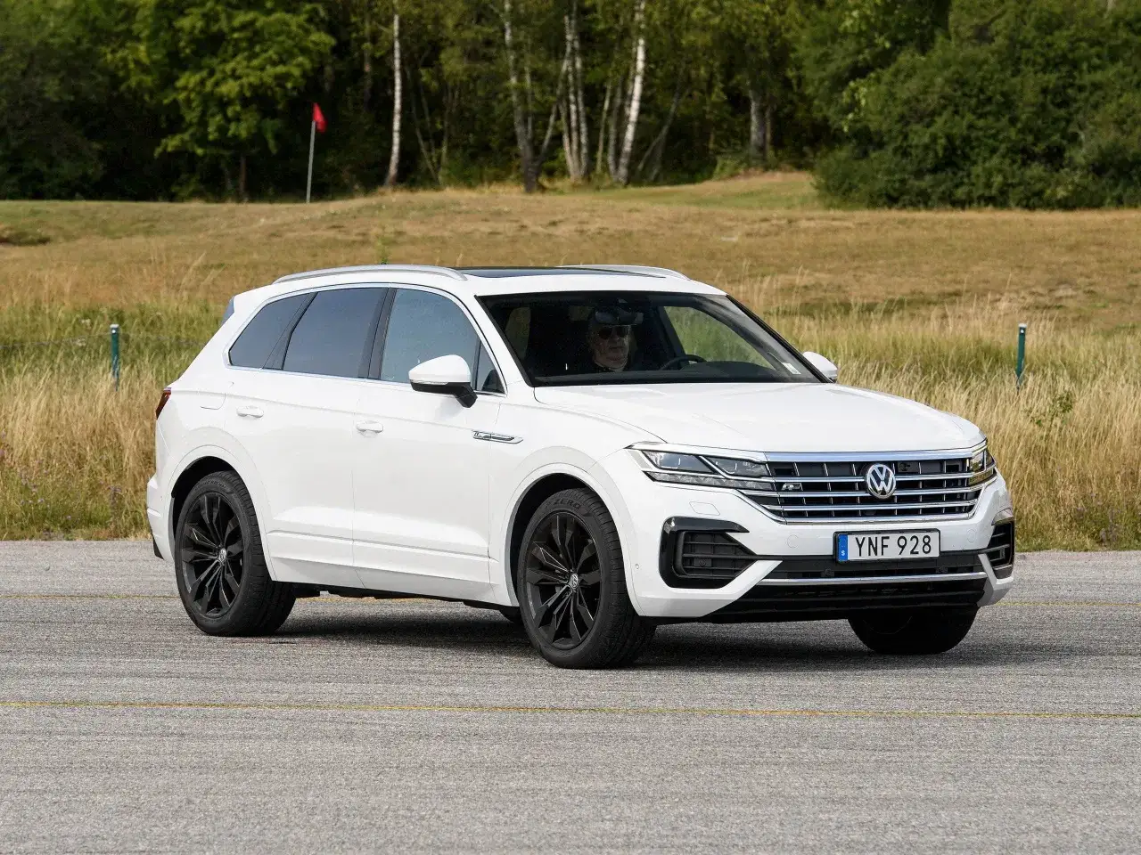 Vit VW Touareg med mörka fälgar kör på en asfalterad yta. En golfbana syns i bakgrunden, kanske ett oväntat ställe för ett vw touareg problem.