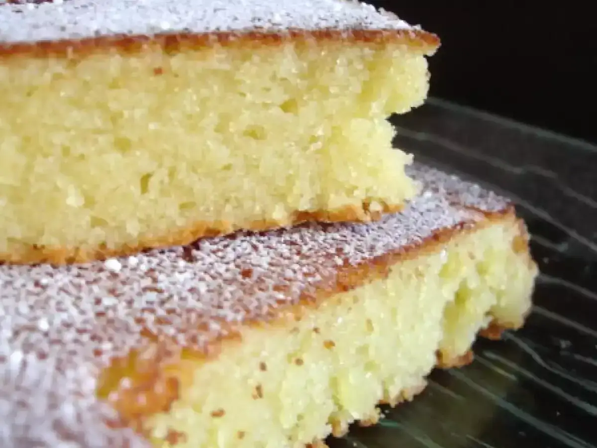 Deux parts de gâteau aux amandes, saupoudrées de sucre glace, sur une assiette en verre.