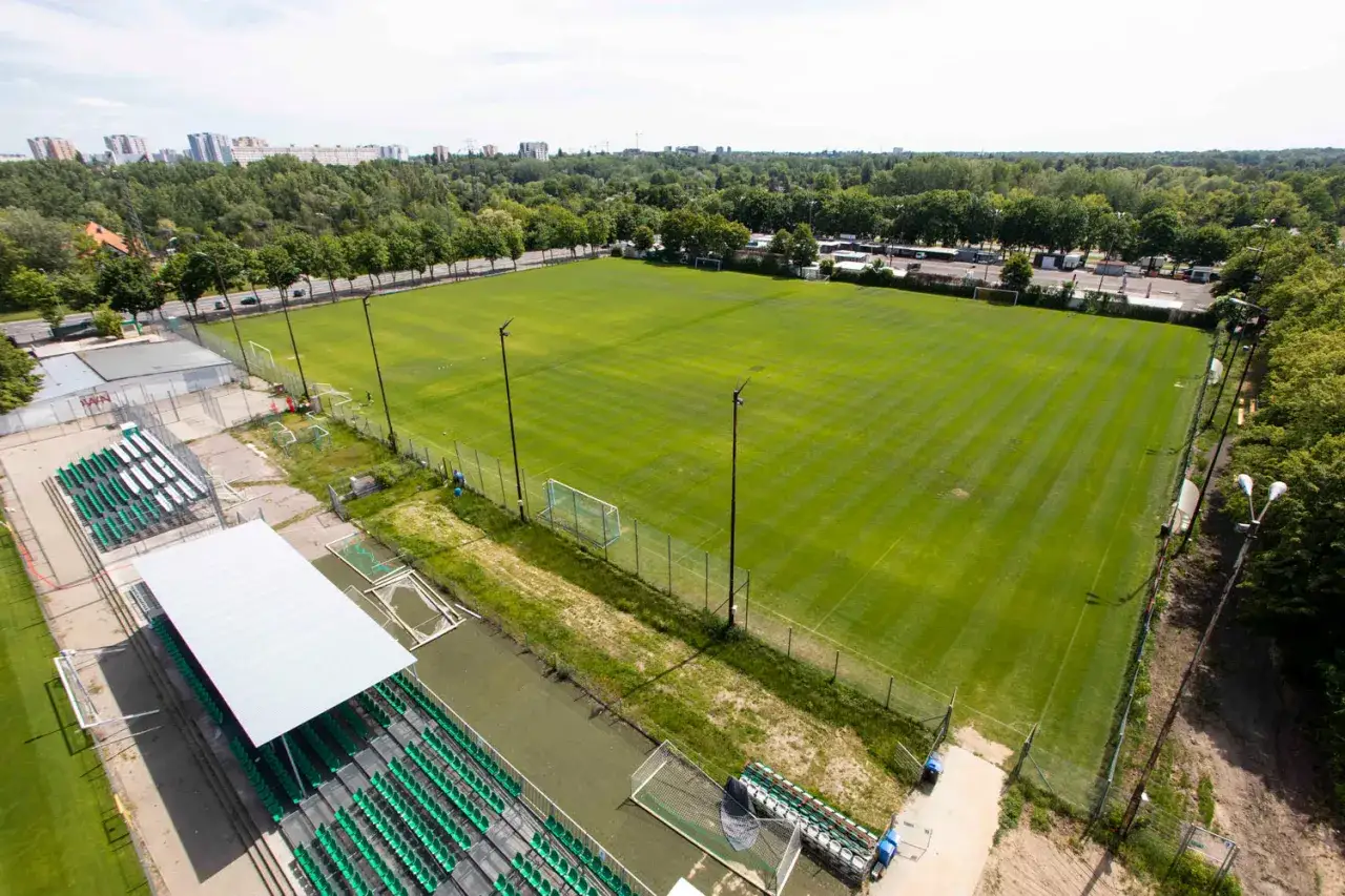 Piękny, zielony teren treningowy na stadionie Warty Poznań. Puste trybuny czekają na kibiców.