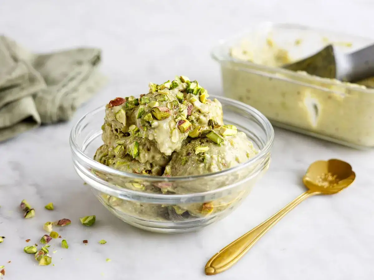 Pistaschglass i skål, perfekt för ett enkelt gelato recept. En guldig sked ligger bredvid.