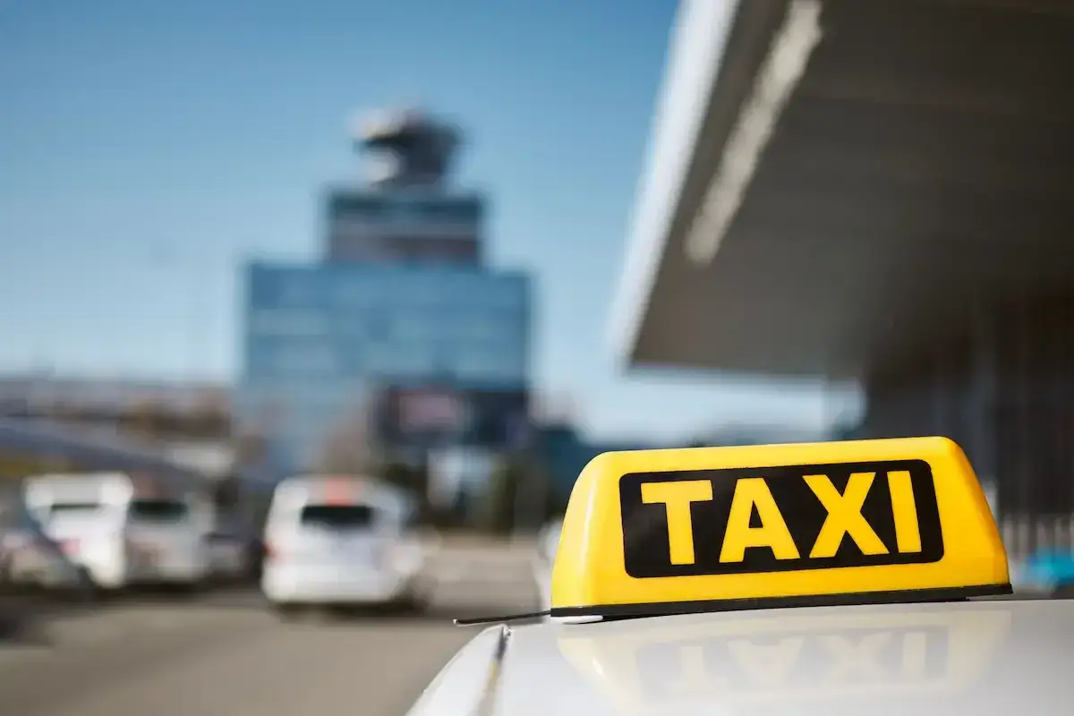 Żółty napis TAXI na dachu samochodu przed budynkiem lotniska.