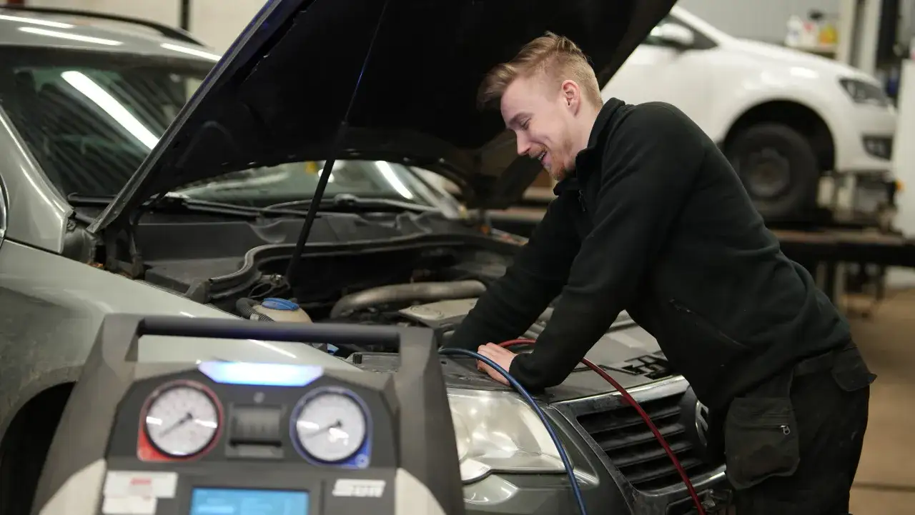 Mekaniker jobbar med att serva bilen, kopplar in utrustning vid motorn.