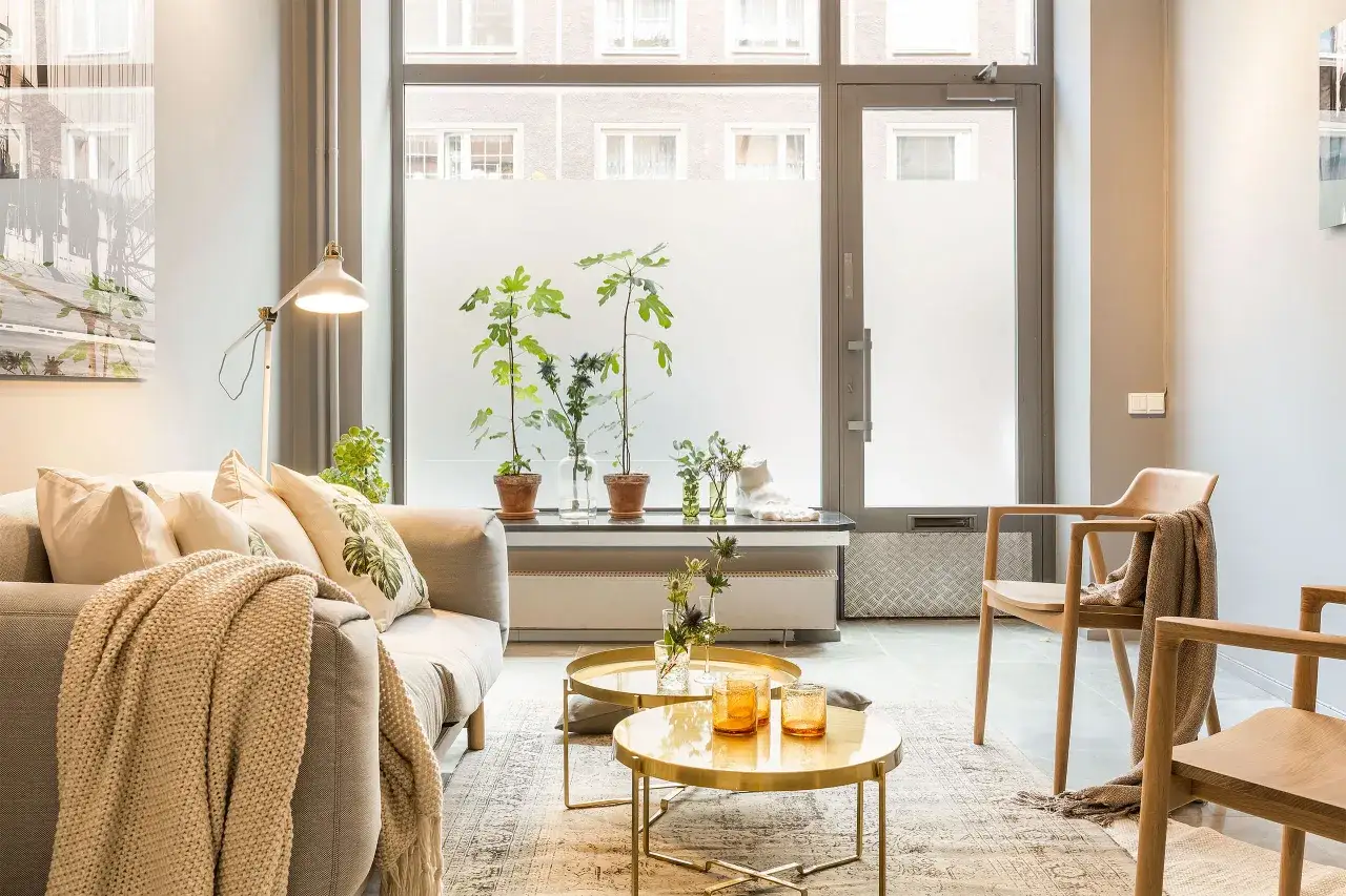 Salon lumineux avec canap&eacute; confortable, tables basses dor&eacute;es et plantes vertes, cr&eacute;ant une ambiance harmonieuse pour une maison feng shui.