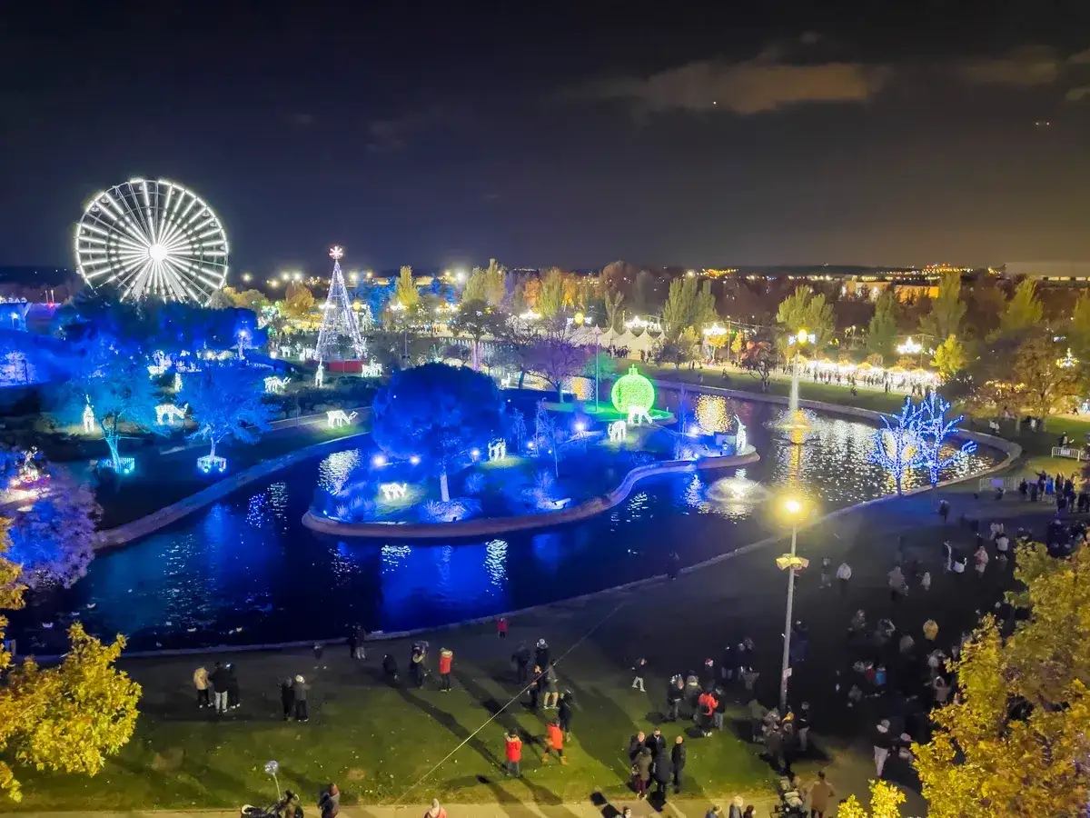 Vista nocturna de la ciudad de la Navidad en Madrid, con noria, árbol iluminado, luces azules y gente paseando.