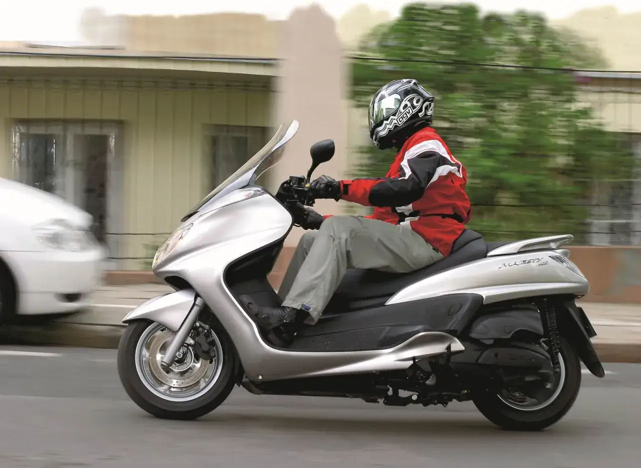 Jazda skuterem Yamaha Majesty 400 po mieście. Kierowca w kasku i czerwonej kurtce.