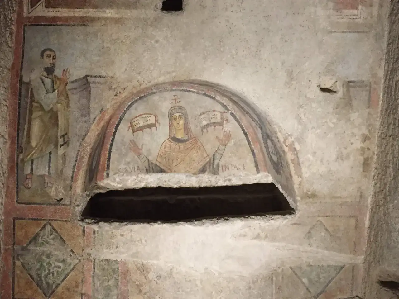 Affresco antico in una tomba, forse la tomba di San Gennaro, con figure sacre e iscrizioni latine.