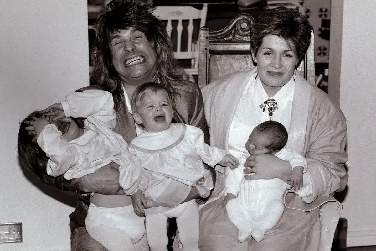 Ozzy Osbourne z żoną Sharon i ich maluchami. Dzieci Osbourne'ów w ramionach rodziców, jedno płacze, drugie się śmieje.