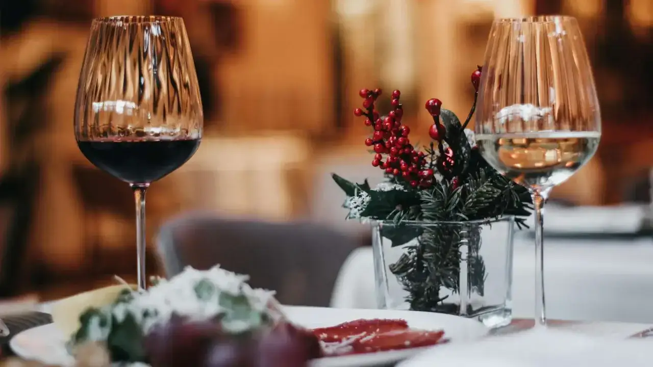 Elegancki stół z kieliszkiem czerwonego wina wytrawnego, ozdobiony zimową kompozycją z jemiołą i gałązkami świerku.