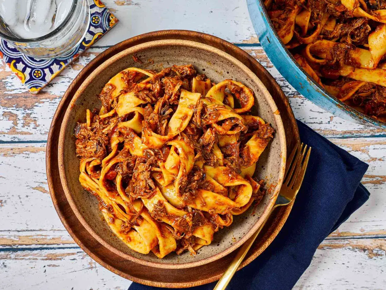 En skål med breda nudlar täckta av en mustig pasta ragu. En kastrull med mer pasta ragu syns i bakgrunden.