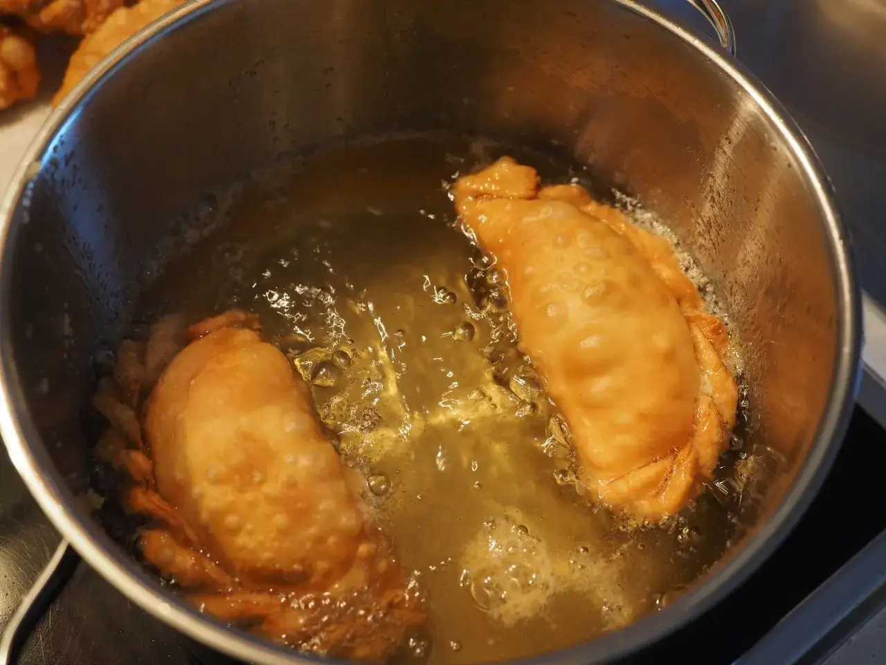 Due calzoni dorati friggono in olio di oliva bollente in una pentola d'acciaio.