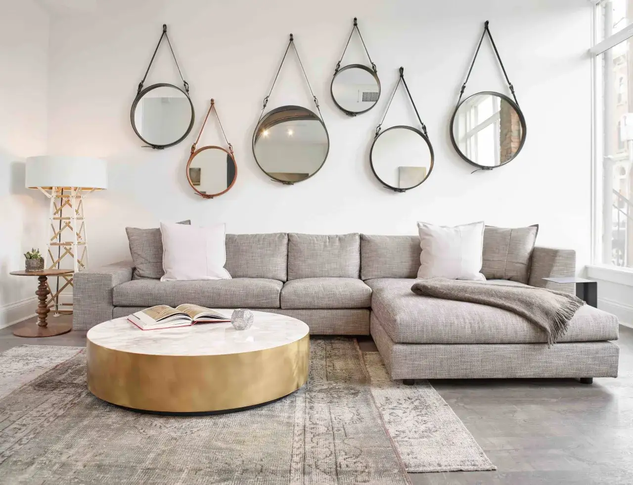 Table basse avec plateau en marbre et base en laiton, un canap&eacute; gris, des miroirs muraux et un tapis.