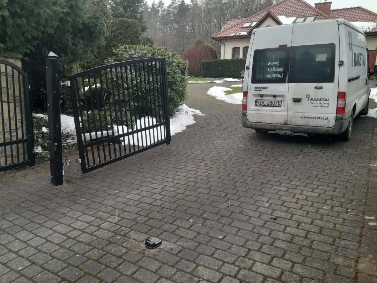 Otwarta brama wjazdowa pod kątem, obok biały van firmy RAKSTAL.