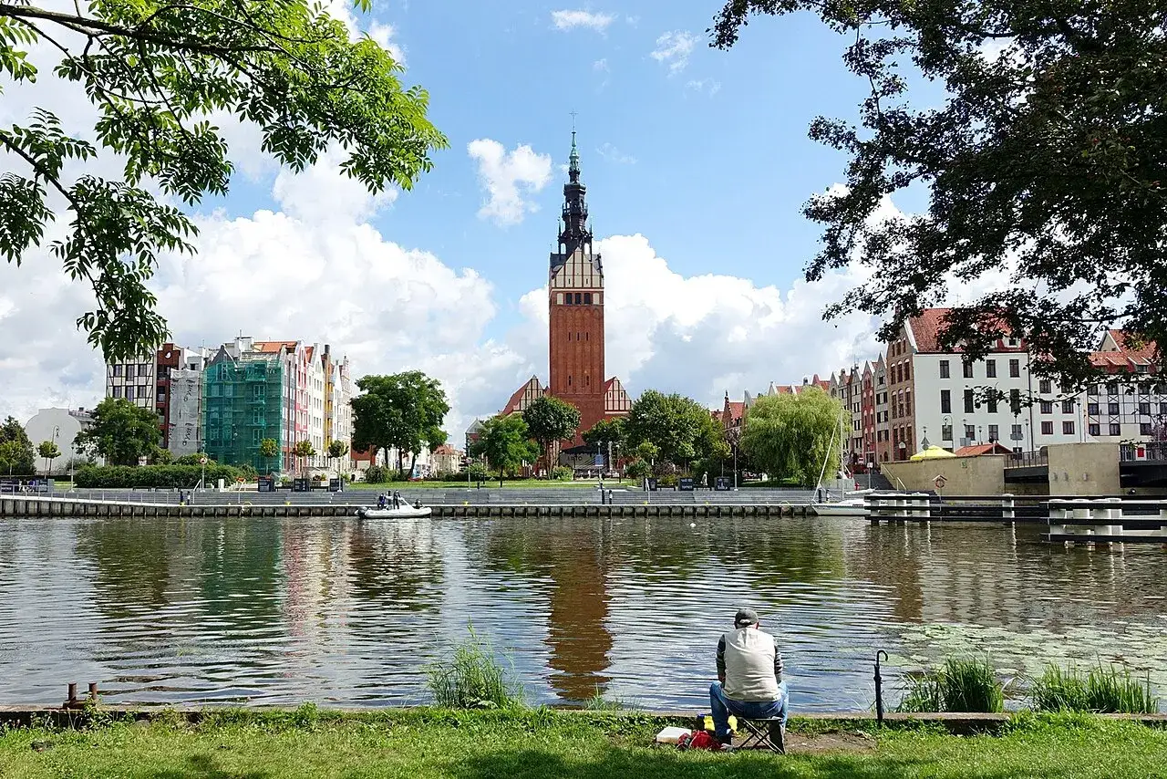 Spokojny wędkarz nad rzeką w Elblągu. W tle widok na zabytkowe kamienice i wieżę Bazyliki. Idealne miejsce, by odkryć elbląg i okolice co zobaczyć.