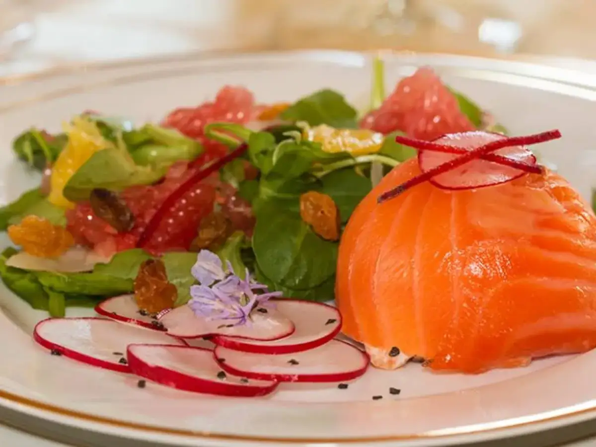Un morceau de saumon fumé, orné de fines lamelles de radis et d'une touche florale, accompagne une salade colorée de pamplemousse et d'agrumes.