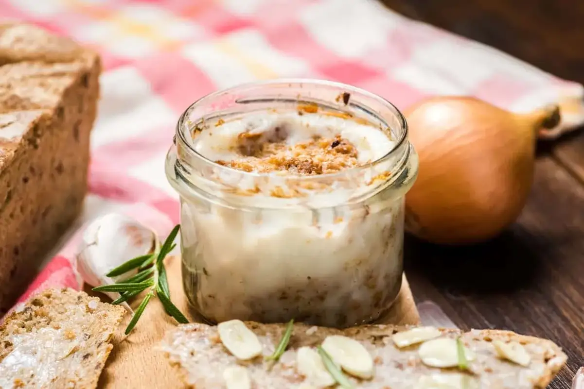 Smalec ze skwarkami w słoiku, obok chleba, czosnku i cebuli. Czy smalec ze skwarkami jest zdrowy? To tradycyjny przysmak.