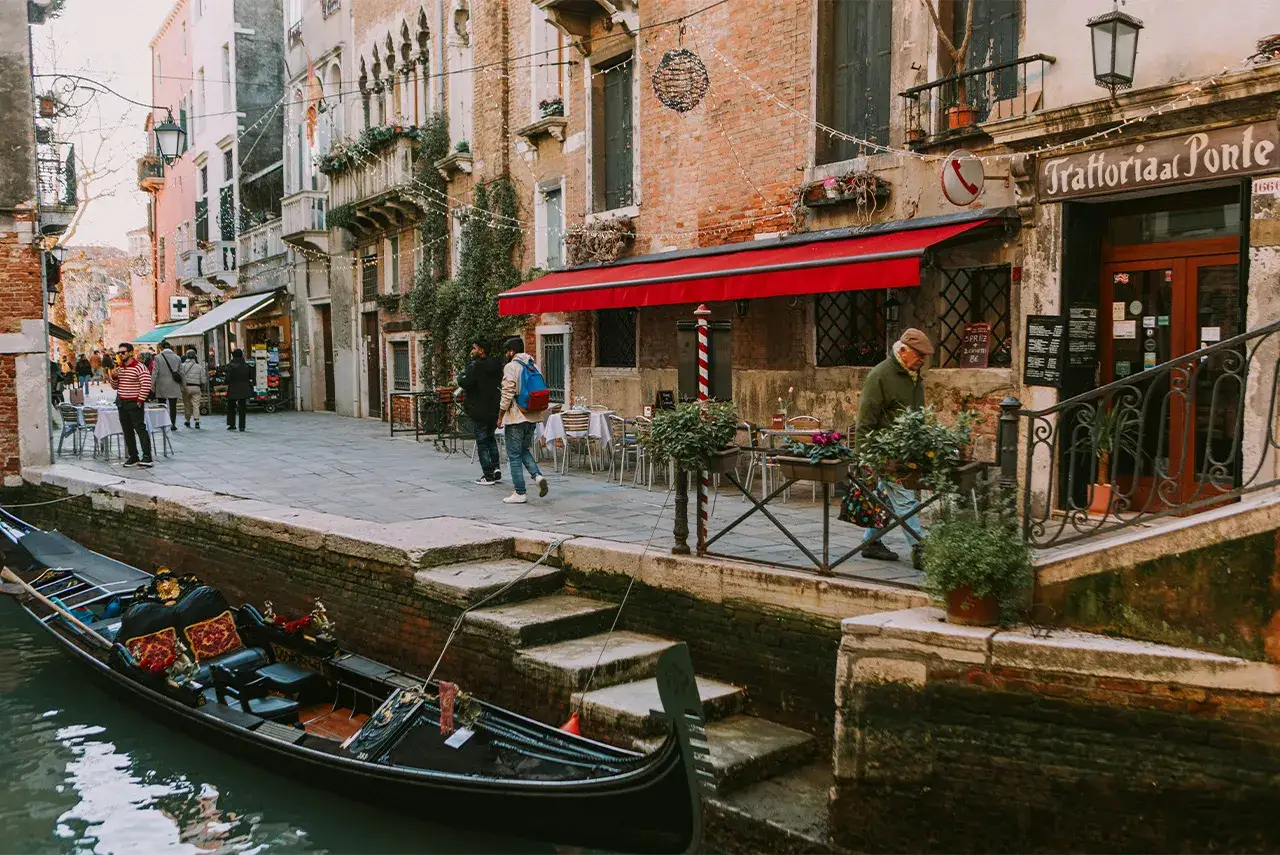 Venezia inverno: gondola ormeggiata, vicoli con negozi e trattorie, gente passeggia.