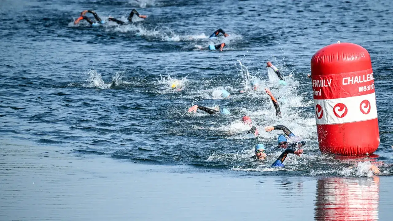Swimmers in a triathlon swim training race navigate choppy water around a red buoy.