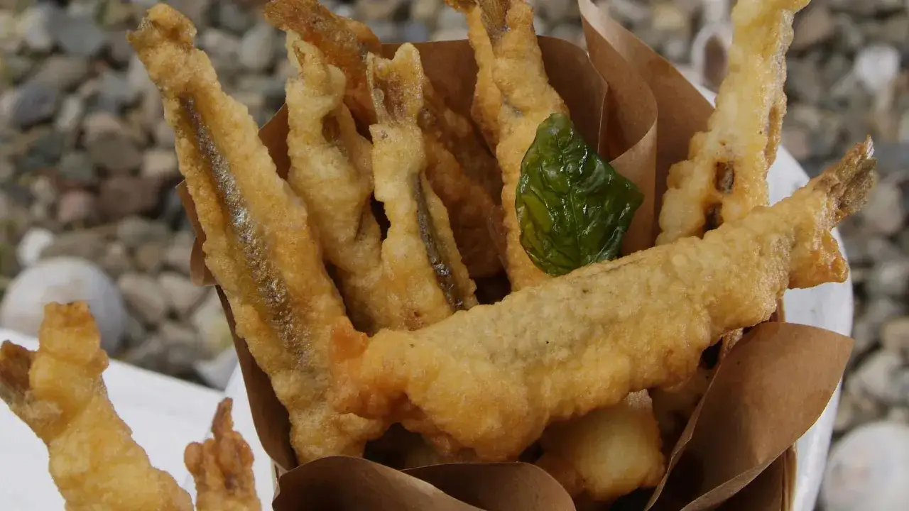 Accras de poisson croustillants, dorés et appétissants, servis dans un cornet en papier brun. Une feuille de basilic apporte une touche de fraîcheur.
