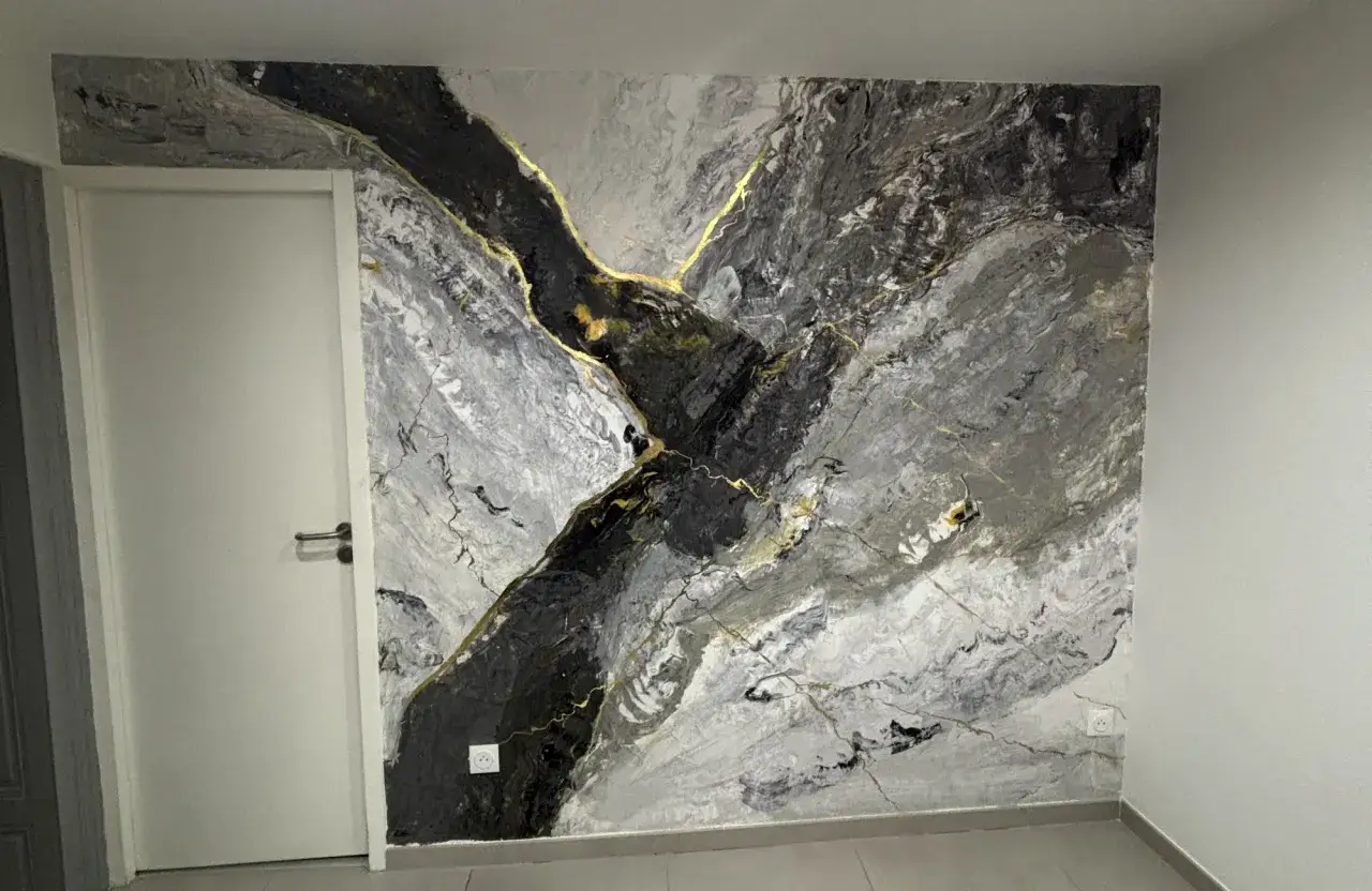 Impression d'art mural en **stucco peinture** aux tons gris et noirs, traversée de veines dorées, évoquant un paysage rocheux abstrait.