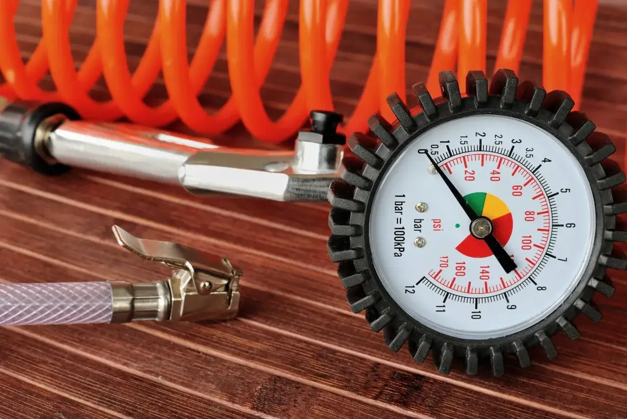 Manometro per gonfiare gomme auto, con tubo a spirale arancione e pinza metallica.