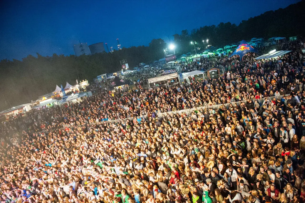 Ein riesiges Publikum feiert beim lautfeuer festival unter dem Nachthimmel. Zelte und B&uuml;hnen sind im Hintergrund zu sehen.