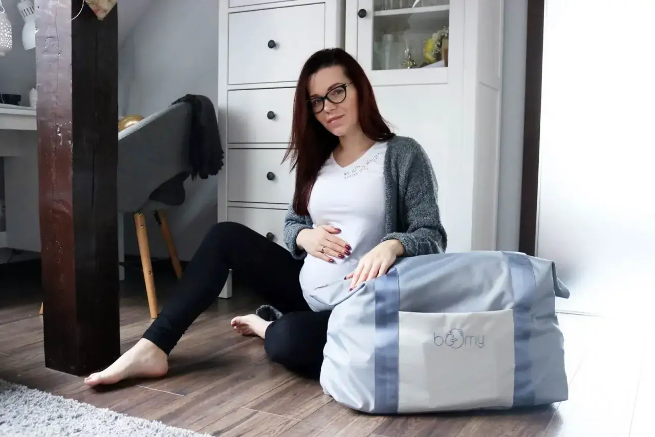Przyszła mama z torbą do porodu, co spakować? Wygodnie usiadła na podłodze, przygotowując się na przyjście dziecka.