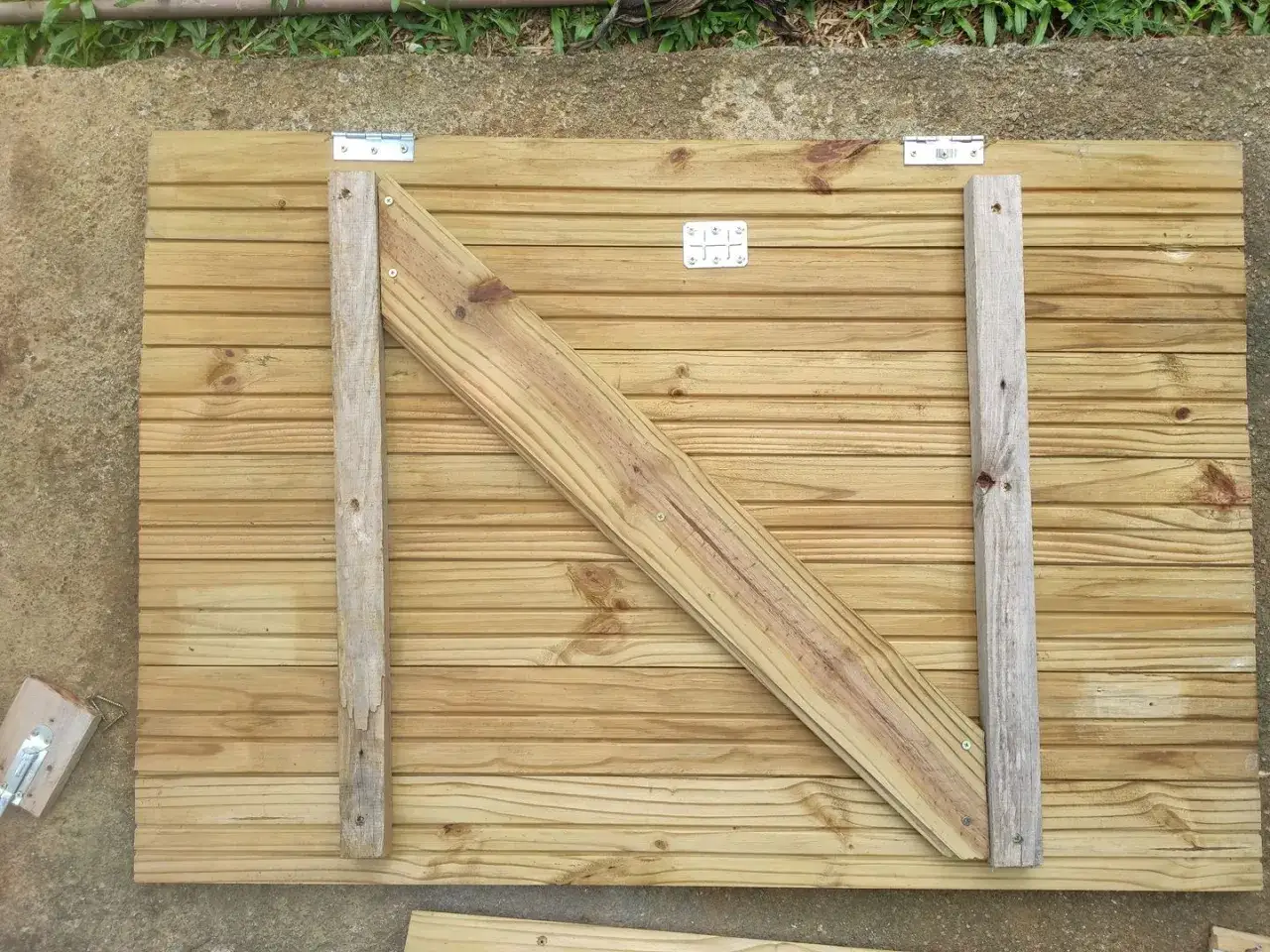 Costruzione di persiane in legno fai da te: pannello in legno con rinforzi diagonali e cerniere, pronto per essere installato.