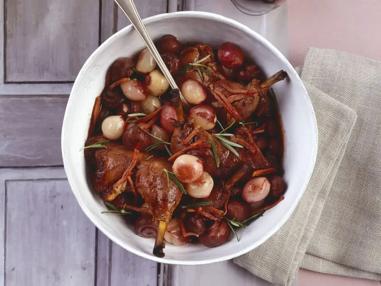 Klassisches Coq au Vin Rezept: Zarte Hähnchenteile in Rotwein geschmort mit Perlzwiebeln, Champignons und Rosmarin.