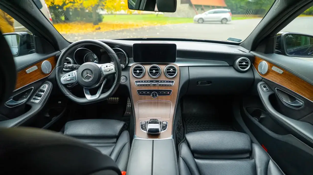 Wnętrze luksusowego **Mercedes C Klasa W205** z drewnianymi wstawkami i czarną sk&oacute;rzaną tapicerką. Widok na deskę rozdzielczą, kierownicę i fotele.
