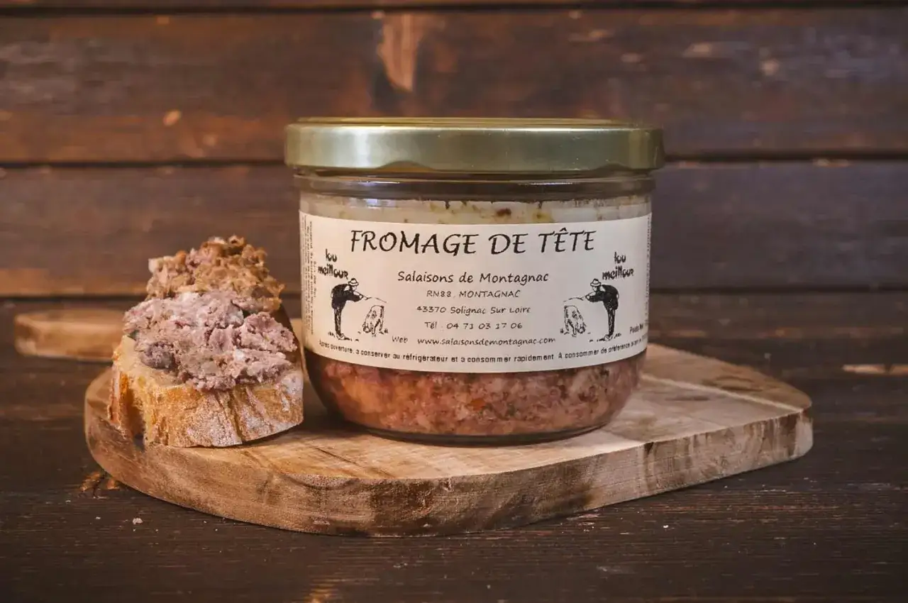 Un pot de fromage de t&ecirc;te artisanal de Salaisons de Montagnac, servi sur une tranche de pain rustique.