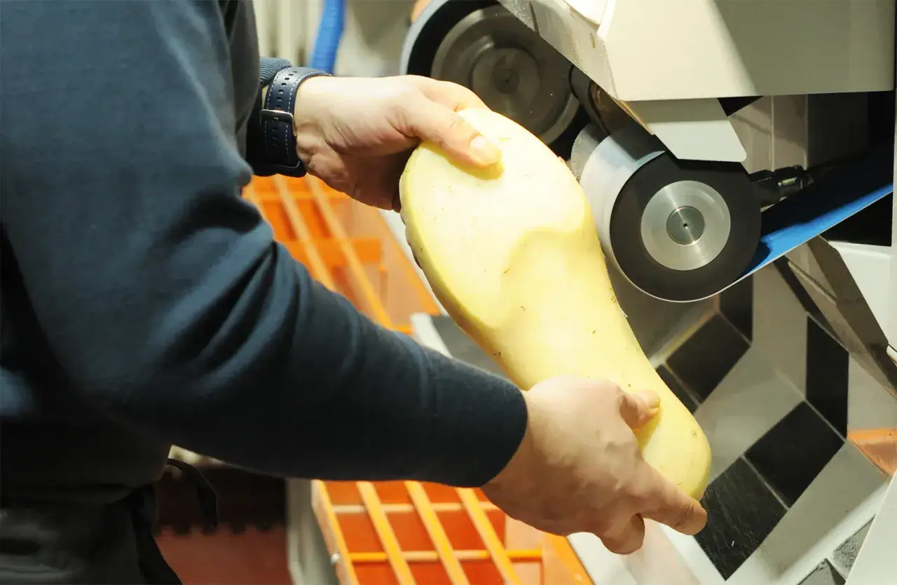 Ein Handwerker formt mit einer Schleifmaschine eine gelbe Einlage. Diese sensomotorische schuheinlagen werden präzise gefertigt.