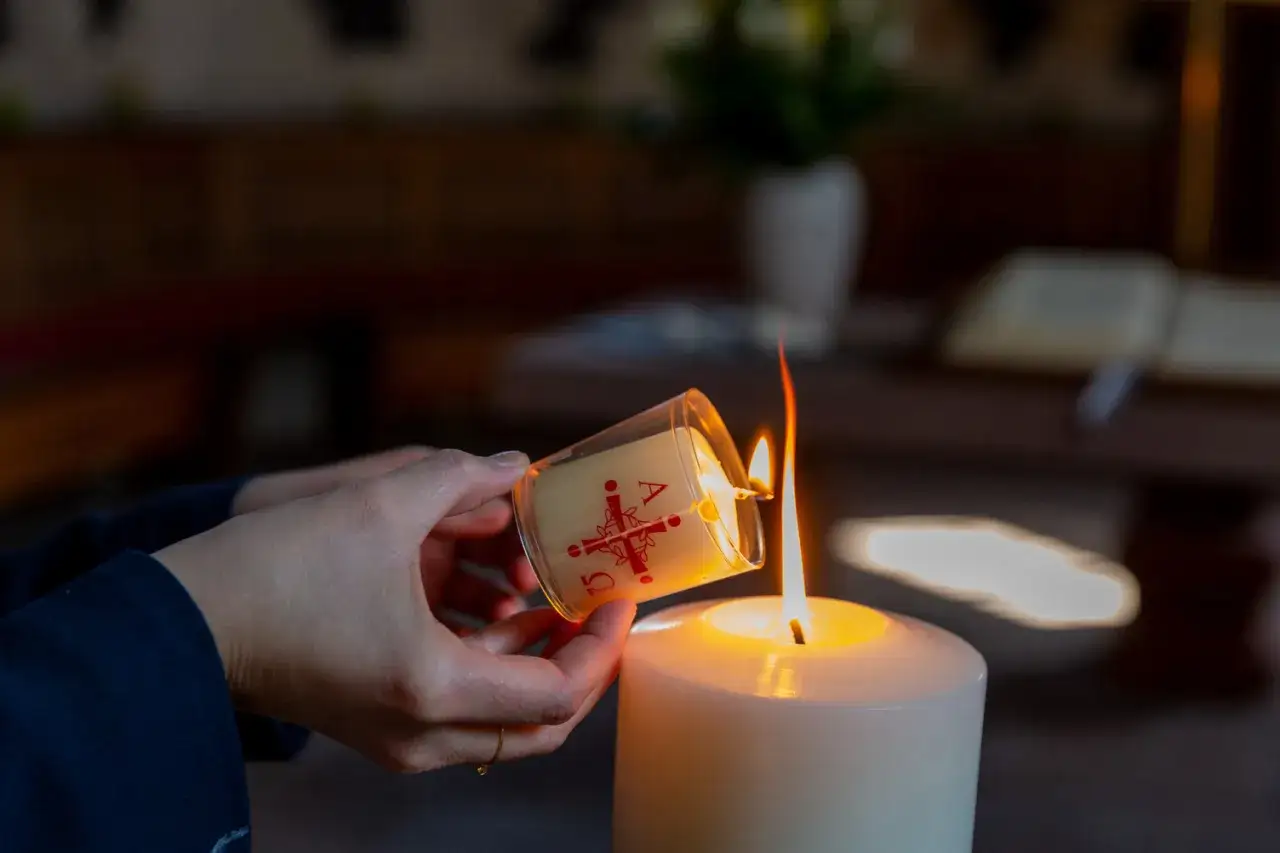 Hände entzünden eine Osterkerze mit dem Alpha und Omega Symbol. Ein Moment des Glaubens im Christentum.