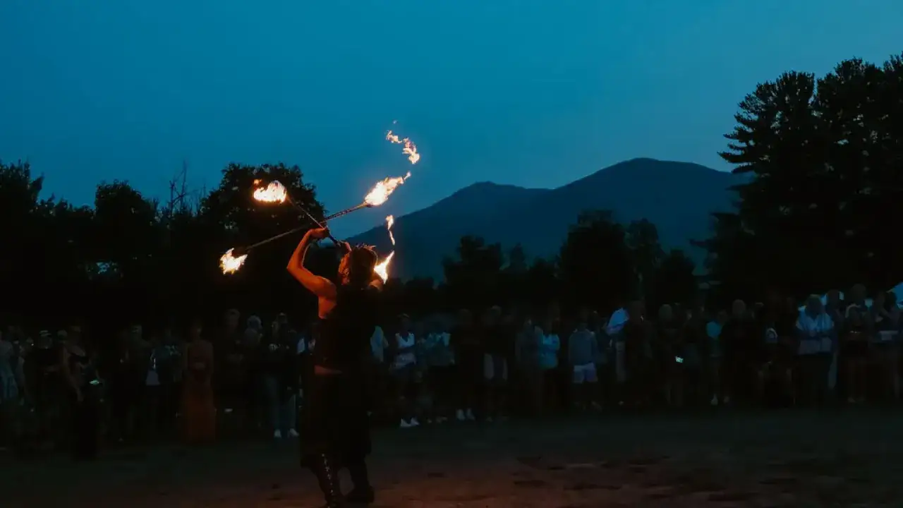 Fire dancer entertains a crowd at the lil dub festival under a twilight sky, with mountains in the background.