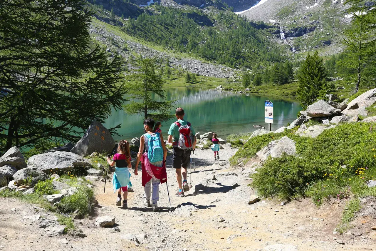 Famiglia in escursione, godendosi le vacanze in montagna con bambini. Un lago alpino cristallino fa da sfondo a questo momento di gioia.