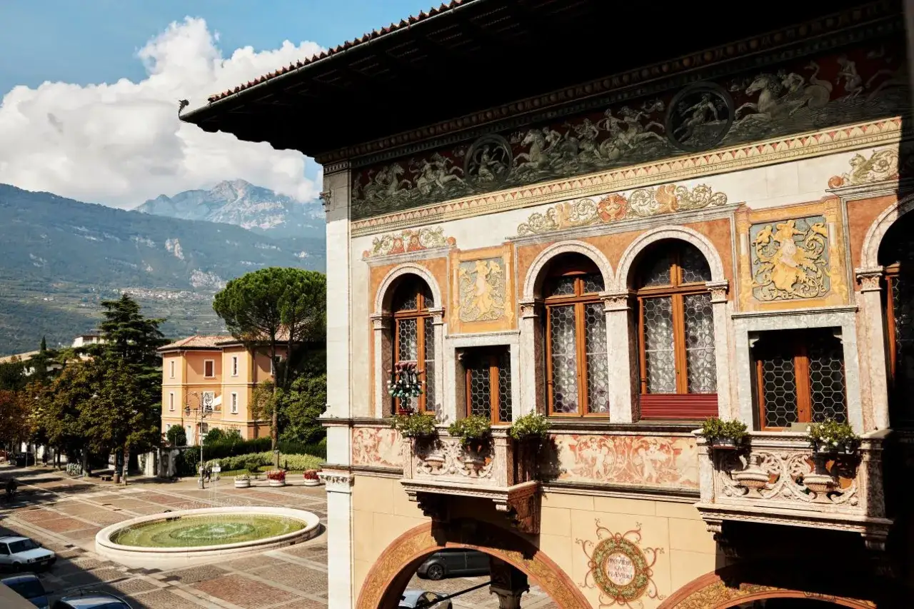 Piazza con fontana e palazzo affrescato, un assaggio di Rovereto cosa vedere. Montagne sullo sfondo.