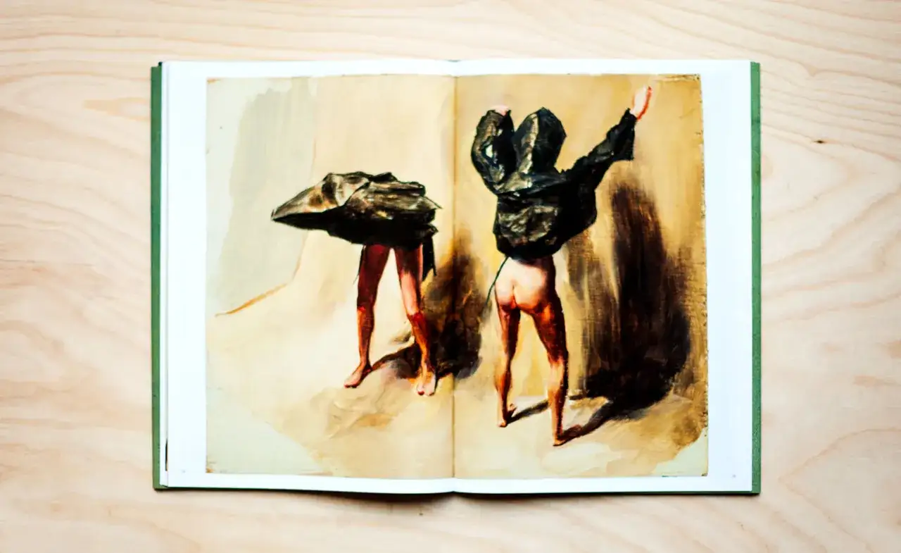 Two figures in a book of Michael Borremans paintings, their bodies obscured by dark, crumpled forms, stand against a muted background.