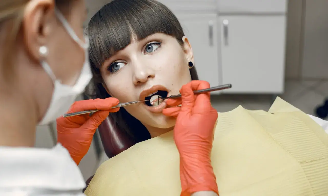 Dentysta w czerwonych rękawiczkach bada ząb pacjentki, na którym widać nową plombę.