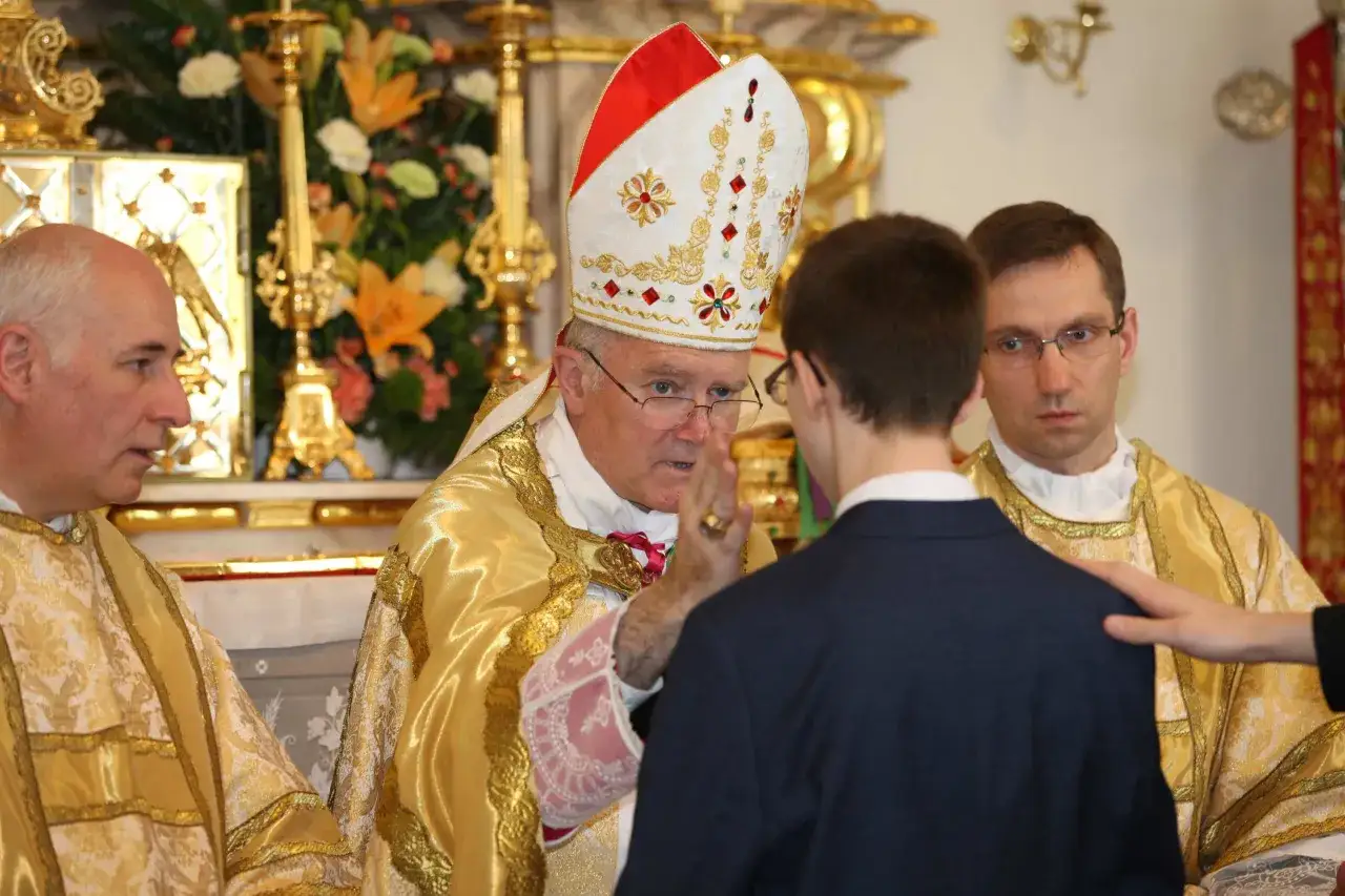 Biskup udziela sakramentu bierzmowania młodemu mężczyźnie. Ceremonia w kościele, choć uroczysta, zazwyczaj nie trwa długo.